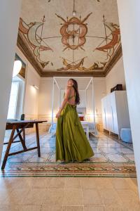 Una mujer con un vestido verde parada en una habitación en Costamante Suites & Spa, en Castellammare del Golfo