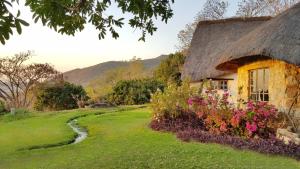 ein Cottage mit einem Strohdach und Blumen in der Unterkunft Wide Horizons Mountain Retreat in Malkerns