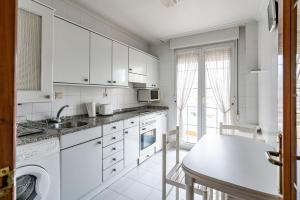 uma cozinha com armários brancos, uma mesa e um lavatório em Piso con Piscina em Santander