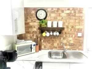 cocina con microondas y reloj en una pared de ladrillo en Nice and Cosy Large Studio near Luton Airport en Luton