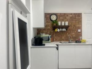 a kitchen with white cabinets and a clock on a brick wall at Nice and Cosy Large Studio near Luton Airport in Luton