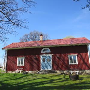 un granero rojo con una puerta y ventanas azules en Huldas gård villa med självhushåll, en Kumla