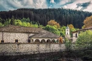 um edifício de pedra com uma torre de relógio e uma igreja em Майоровата къща em Shiroka Lŭka