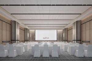 une salle de conférence avec des tables et des chaises blanches et un écran dans l'établissement Qingdao Marriott Hotel Jiaozhou, à Qingdao