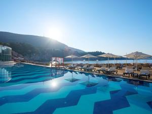 a swimming pool with chairs and umbrellas next to the water at Rixos Premium Dubrovnik in Dubrovnik