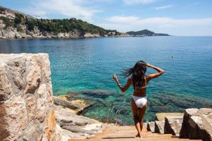 a woman in a bikini walking down a wooden path towards the water at Rixos Premium Dubrovnik in Dubrovnik