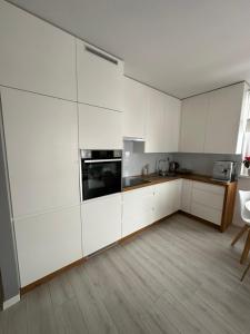 a white kitchen with white cabinets and a wooden floor at Apartament Szczytno Zielona in Szczytno