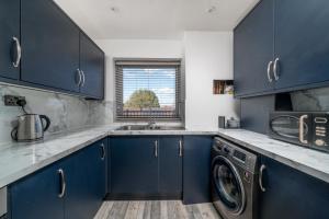 cocina con armarios azules y lavadora en Private Room in London Enfield with parking, en Enfield