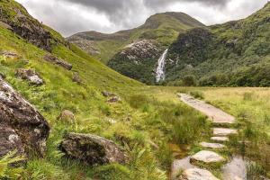 a path in a field with a waterfall in the mountains at Fort William - Highland holiday home in Fort William