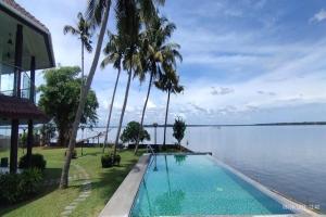 a swimming pool with palm trees next to a body of water at Waters Edge Kochi - a VKation Experience in Cochin
