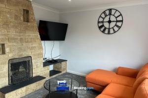 a living room with an orange couch and a clock at 3 Bedroom Cosy Bungalow By Beds Away Short Lets & Serviced Accommodation Chalgrove With Outdoor Dining Area 