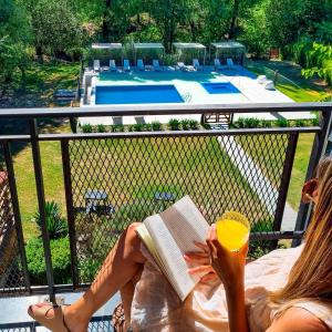 una mujer sentada en un balcón leyendo un libro y tomando una copa en Atelier Hotel de Charme en Villa General Belgrano