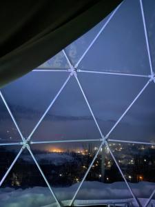 una vista a través de una ventana de cristal de una ciudad por la noche en 4 seasons. 4 სეზონი Glamping Georgia Racha en Ambrolauri