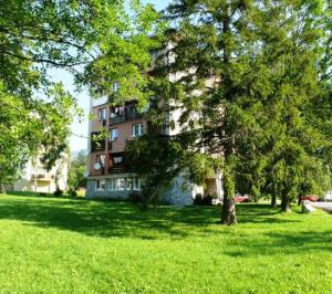 un edificio en un parque con árboles delante de él en Apartman Dinda, en Tatranská Lomnica