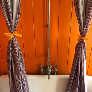 a bath tub with curtains in front of an orange wall at Beautiful 18th Century Old Rectory with river in Norwich