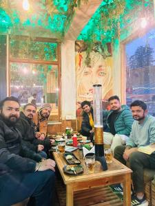 un grupo de hombres sentados alrededor de una mesa en una habitación en The Mad King's House & Cafe, en Manali