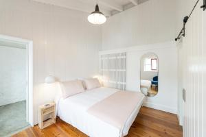 a white bedroom with a bed and a mirror at Engenho Hostel in Lajes do Pico