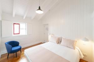 a white bedroom with a bed and a blue chair at Engenho Hostel in Lajes do Pico
