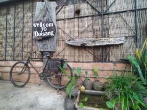 una bicicleta estacionada al lado de una pared con un cartel de bienvenida al muelle en Doi Sang Farm Stay - ดอยซางฟาร์มสเตย์, en Ban Huai Kom