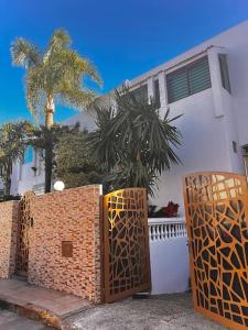 a white house with a fence and a palm tree at Nassali - Luxurious Beachfront Villa with Private Pool in Casablanca