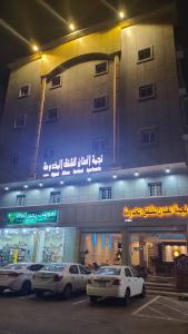 un edificio con coches estacionados en un estacionamiento por la noche en نجمة العنان للشقق المخدومة en Tabuk