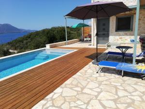 a swimming pool with a wooden deck and an umbrella at Villa VaKo in Vathí