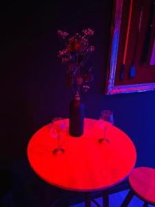una mesa roja con dos vasos y un jarrón con flores en Chambre Noire, en Solre-le-Château