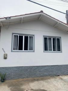 Una casa blanca con dos ventanas. en Casa completa - Governador Celso Ramos à 15m da praia de palmas, en Governador Celso Ramos