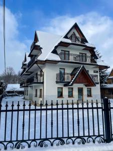 a house with a snow covered roof behind a fence at Willa Lasak in Biały Dunajec
