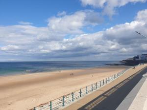 a beach with people walking on the sand and the ocean at Seaviews Apartment, Whitley Bay Sea Front in Whitley Bay