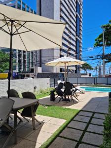 un patio con mesas y sombrillas junto a una piscina en BOA VIAGEM FLAT 106, en Recife