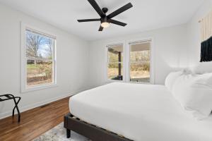 a white bedroom with a ceiling fan and windows at Sage Lodge by AvantStay 15 Min to Downtown Deck in Asheville
