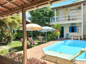 uma piscina com uma cadeira e um guarda-sol e uma casa em Pousada Cajueiro em Itaúnas