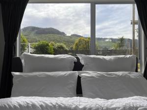Hill View Abode Tawa في ويلينغتون: سرير مع وسائد بيضاء أمام النافذة