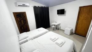 een witte slaapkamer met een bed en een televisie bij Maresias Suítes in Maresias