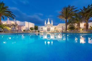 a large swimming pool in front of a church with palm trees at Alua Suites Fuerteventura - All Inclusive in Corralejo