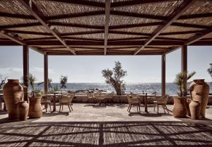 eine Terrasse mit Tischen und Stühlen und Meerblick in der Unterkunft Numo Ierapetra Beach Resort Crete, Curio Collection Hilton in Ierápetra