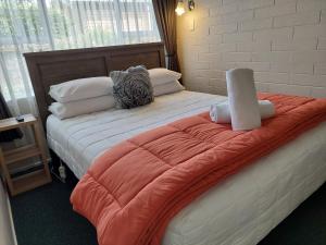 a bed with an orange blanket and pillows on it at Colonial on Tay in Invercargill