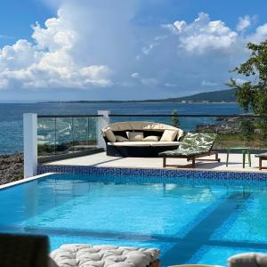 a swimming pool with a couch and chairs next to the ocean at Oceanview lux Villa + Infinity pool, Chef & Butler in Kings Pen