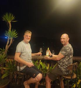 Dois homens sentados numa mesa com copos de vinho. em Monkey Homestay & Bar em Tân Hiệp