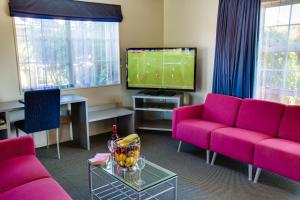 sala de estar con muebles de color rosa y TV de pantalla plana. en ASURE Colonial Lodge Motel, en Napier