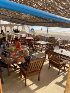 HOTEL DU BAR DE LA MER CAP SKIRRiNG في Kabrousse: مجموعة من الناس يجلسون على الطاولات على الشاطئ