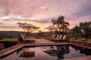 Duas cadeiras e guarda-sóis sentados ao lado de uma piscina em Ekuthuleni Lodge em Welgevonden Game Reserve