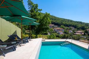 a swimming pool with chairs and umbrellas next to a building at PERUNIKA BED & BREAKFAST in Mošćenička Draga