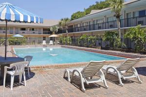 einen Pool mit Stühlen und einem Tisch sowie ein Gebäude in der Unterkunft Days Inn by Wyndham Gainesville University in Gainesville