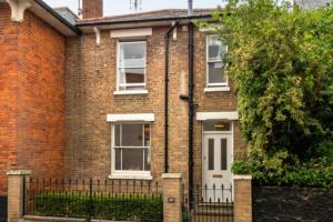 een stenen huis met een witte deur en een hek bij The Cosy Cottage in Litcham