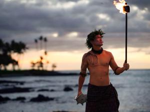 Un uomo a torso nudo sulla spiaggia con una torcia in mano. di Fairmont Orchid a Waikoloa