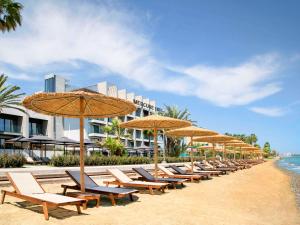 una fila de sillas y sombrillas en una playa en Mercure Larnaca Beach Resort en Lárnaca