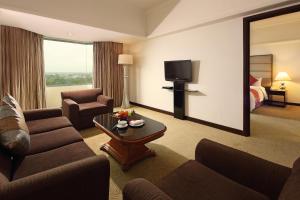 una sala de estar con sofás y TV en una habitación de hotel en Aryaduta Pekanbaru, en Pekanbaru