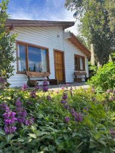 a small white house with windows and purple flowers at Cabaña La Elisa in Villa La Angostura